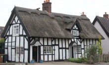 Big old black and white house with thatched roof
